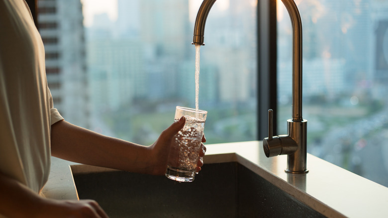 A person holds a glass beneath a faucet and fills it with water