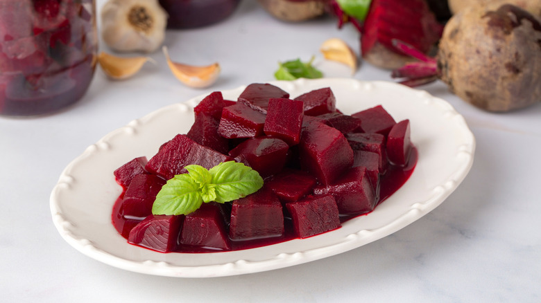 White platter of cubed beets surrounded by raw, whole beets.