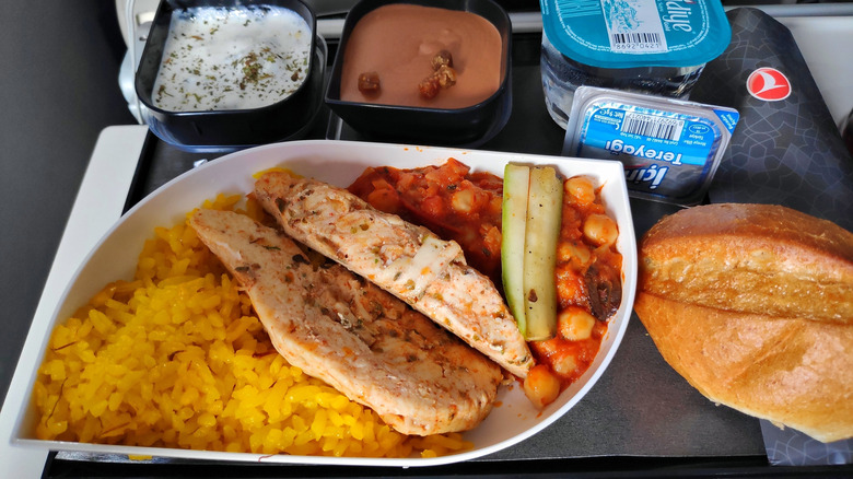 In-flight meal of an entree with rice, vegetabes, bread, and dessert