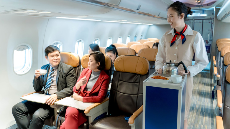 Flight attendant pushing airplane food cart past passengers in seats