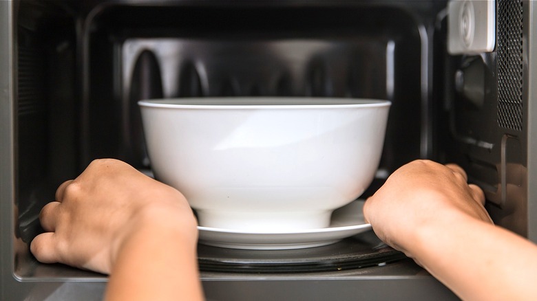 hands putting bowl into microwave