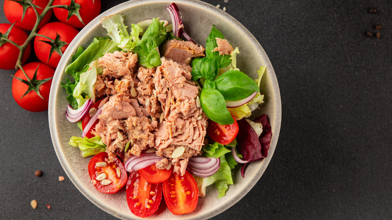 The contents of a can of tuna atop a salad with lettuces, tomatoes, and red onions