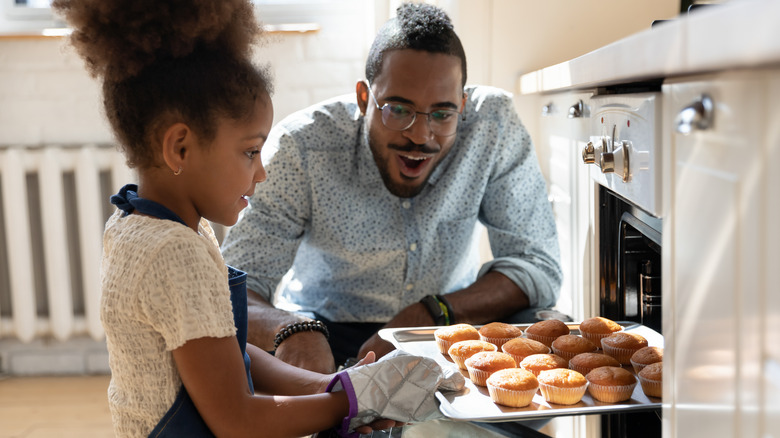 Child pulls muffins out of oven, dad watches