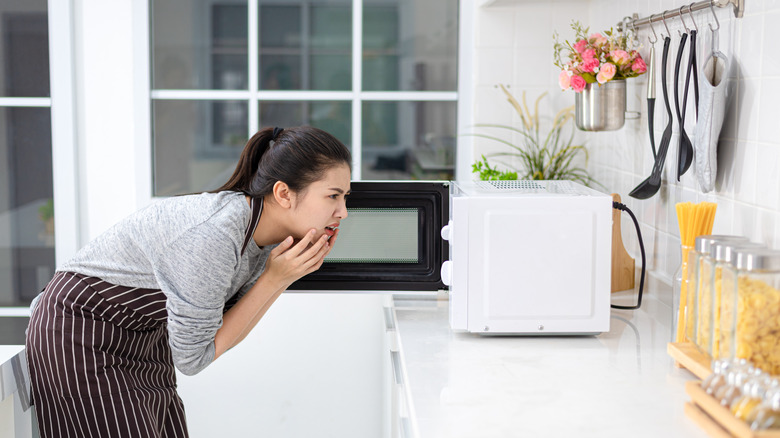 A woman leaning in front of a microwave with her hands touching her exasperated face
