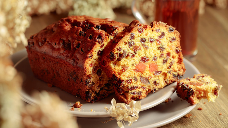 A sliced fruitcake filled with raisins, dried fruits, and nuts on a white plate over a wooden table