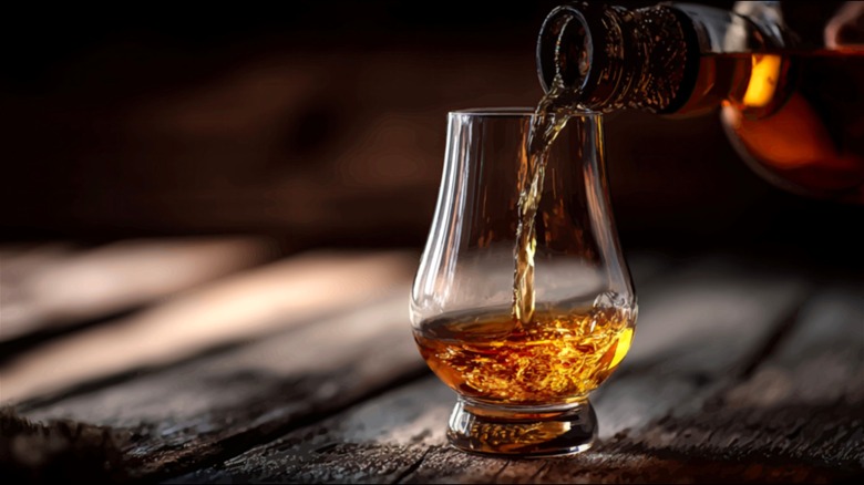 Bourbon being poured into a Glencairn glass on a wooden table.
