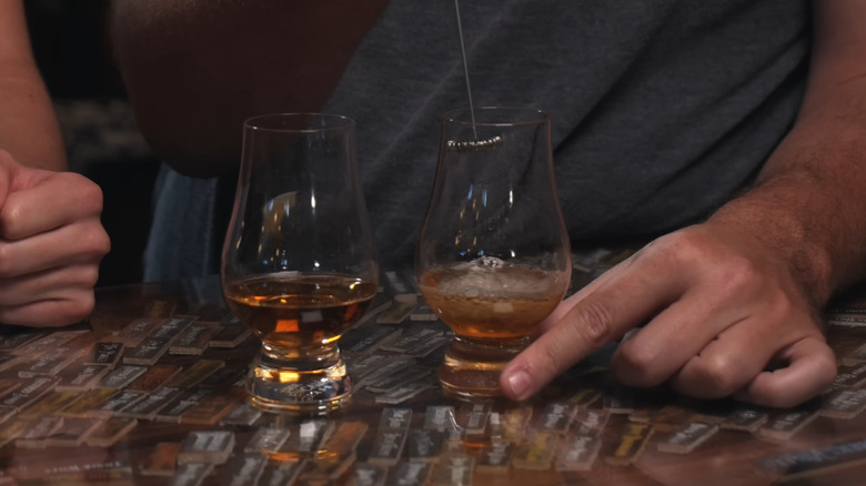 Two glasses of bourbon, with one being agitated by a milk frother and the other left untouched.