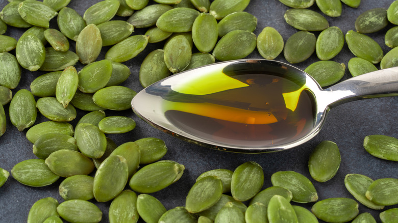 A metal spoon full of pumpkin seed oil sits in a pile of pumpkin seeds