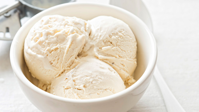 A bowl filled with three scoops of vanilla ice cream, with an ice cream scoop and a spoon