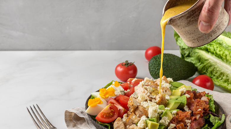 hand pouring dressing on salad