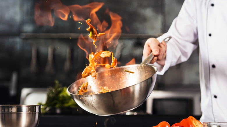 Chef tossing flaming food in wok 