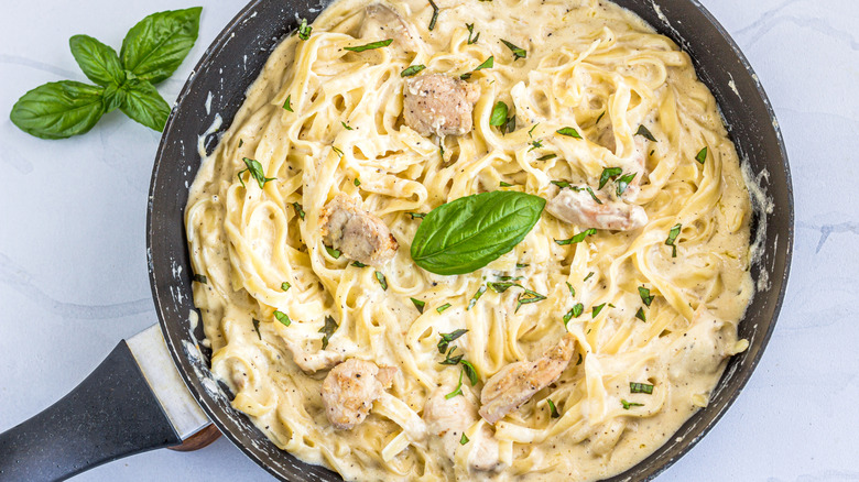 A skillet filled with noodles and meat covered in a cream sauce topped with herbs
