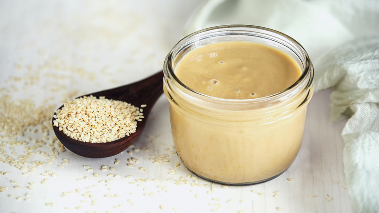 A spoon full of sesame seeds and a jar of tahini sit side-by-side