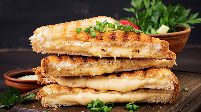 A stack of grilled cheese sandwiches sitting on a wooden cutting board.