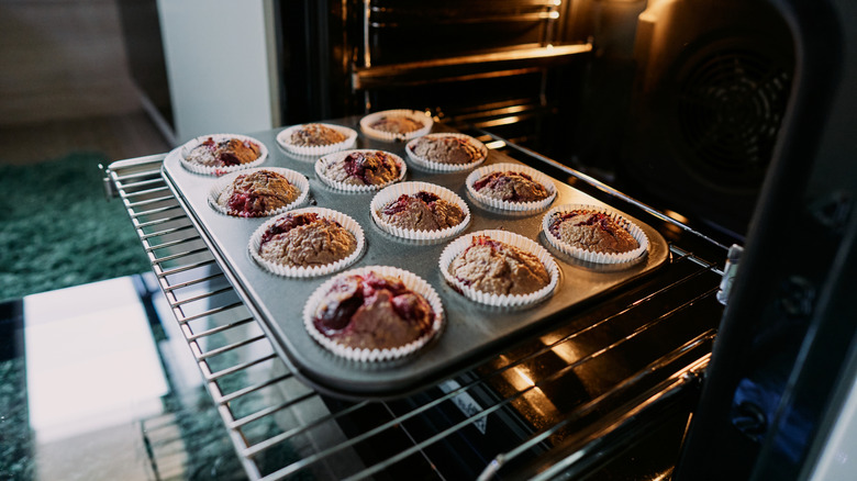 An oven's rack is pulled out, with a tin of chocolate and cherry muffins sitting on it.