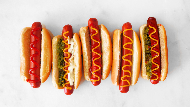 Five hot dogs stuffed inside buns with various toppings including ketchup, mustard, onions, and relish.