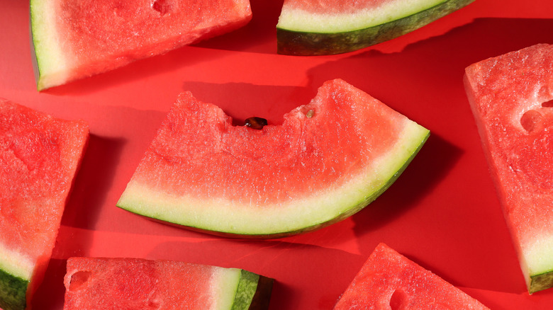 Fresh-cut slices of watermelon, the middle one with a bite taken out of it, on a red surface