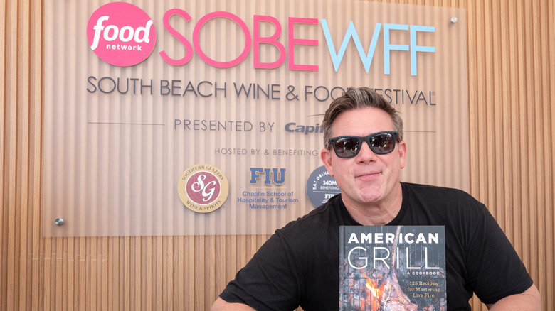 Tyler Florence smiling in front of Food Network sign with his book "American Grill"