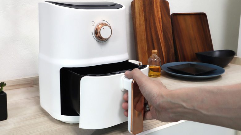 Hand removing basket from white air fryer on kitchen counter.