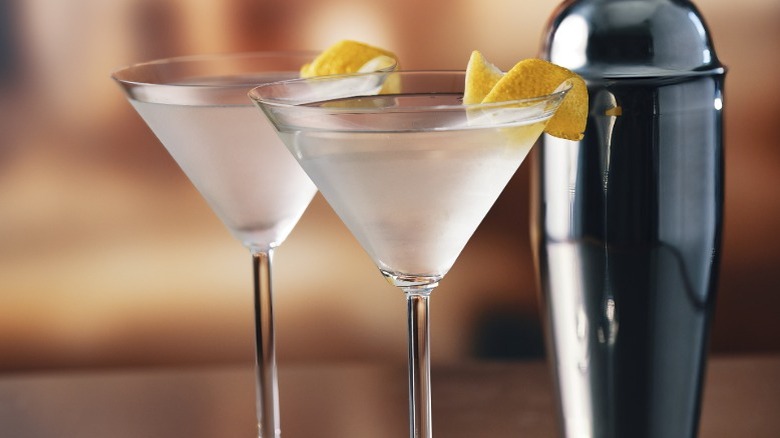 Two gin martinis with lemon wedges in martini glasses, next to a cocktail shaker