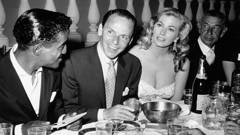 Frank Sinatra smiles as he sits with his entourage at a restaurant.