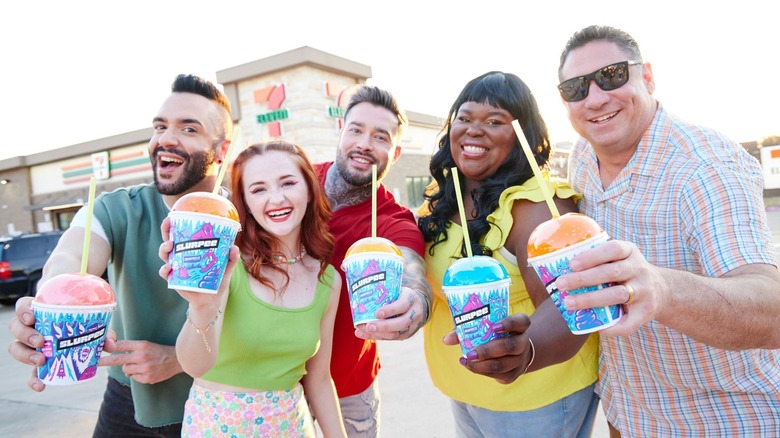 A group of people holding up slurpees in front of 7 Eleven