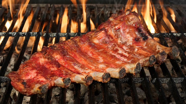 Baby back ribs, smothered in barbecue sauce, cooking on an open flame grill.