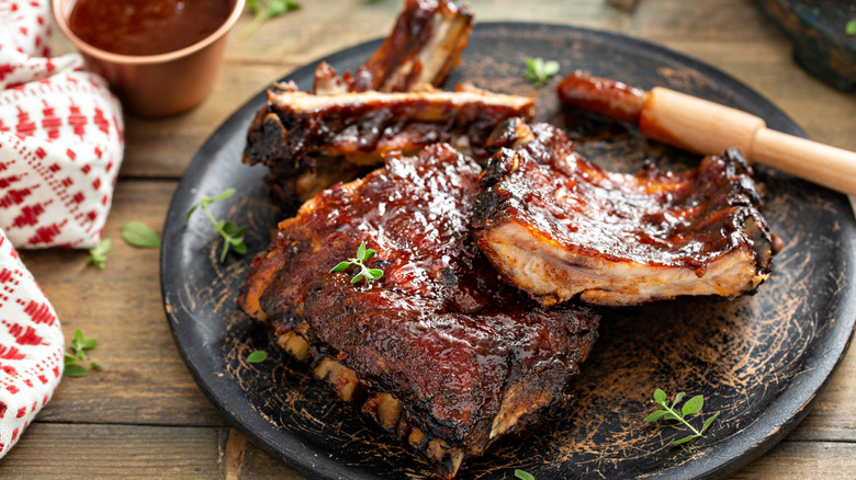 Barbecued ribs on a plate covered in barbecue sauce.