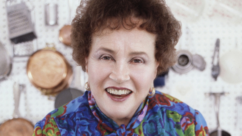 Julia Child smiling with pots and pans hanging on wall in background