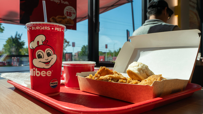 Biscuits, soda, sides, and fried chicken on a tray in a Jollibee restaurant.