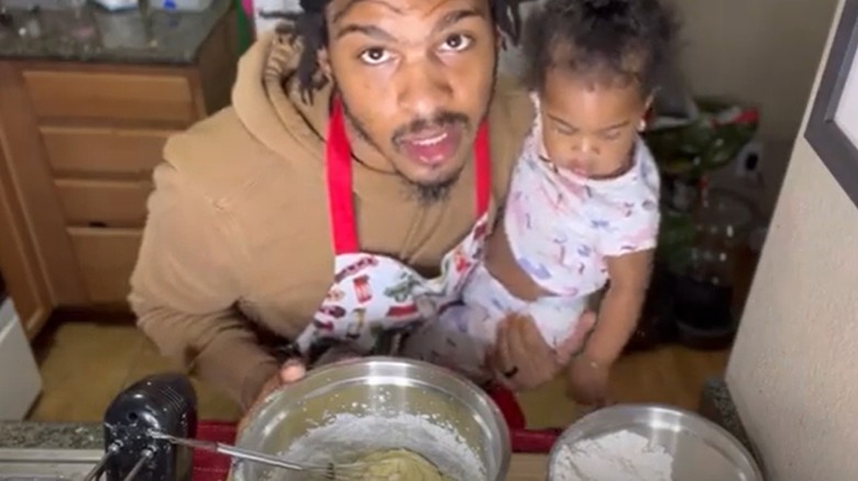 Keith Lee cooking while holding daugter