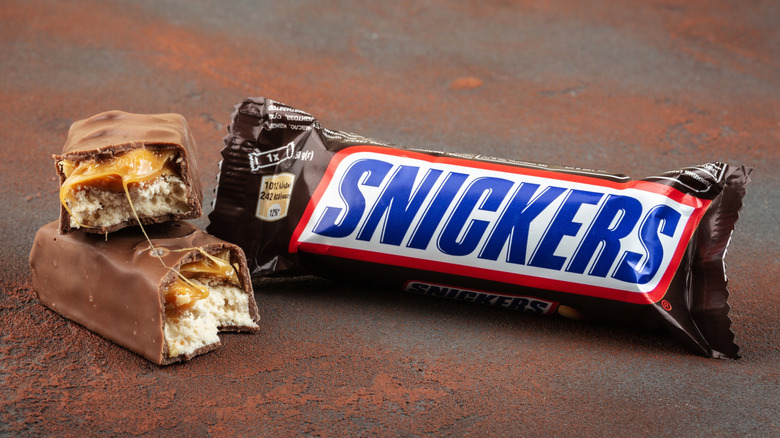A broken unwrapped Snickers bar next to an unopened Snickers bar