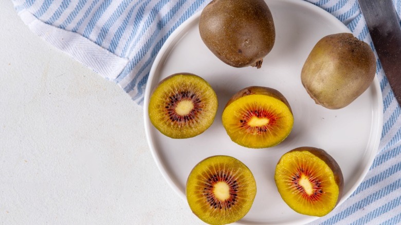 Halved golden kiwis on white plate with two whole kiwis.