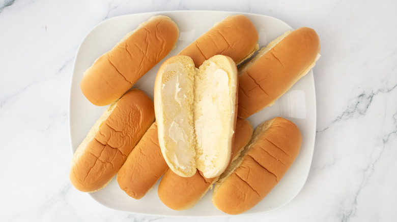 Hot dog buns on plate with one opened and buttered on top