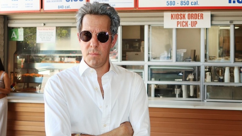 Comedian Jonathan Kite wearing a white shirt and sunglasses in front of a Costco food counter