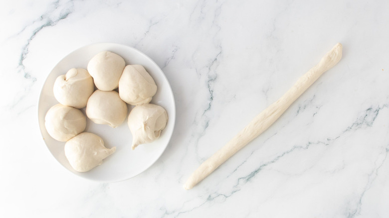 Pizza dough balls on plate next to long dough strip on counter