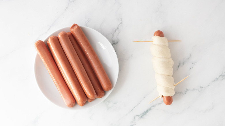 Hot dogs on plate next to dough-wrapped hot dog secured with toothpicks