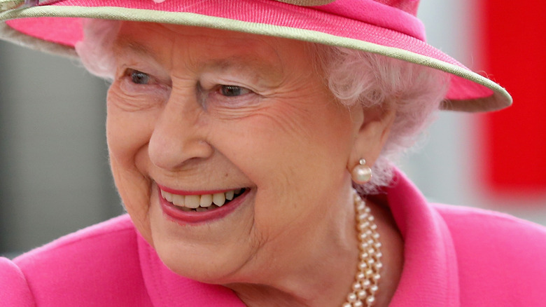 Queen Elizabeth II smiling and wearing pink hat