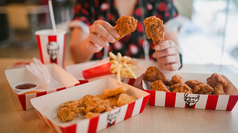 hands holding chicken pieces with various KFC meals on the table