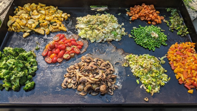 Piles of vegetables cooking on a Blackstone griddle