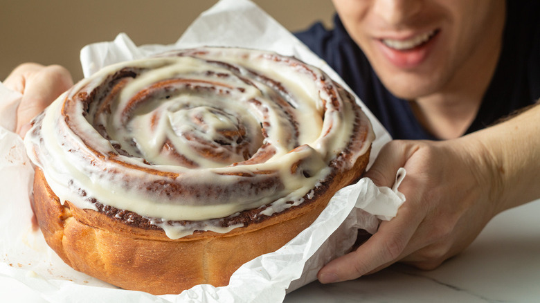 giant cinnamon roll held in a pair of hands on a table near plates and a knife