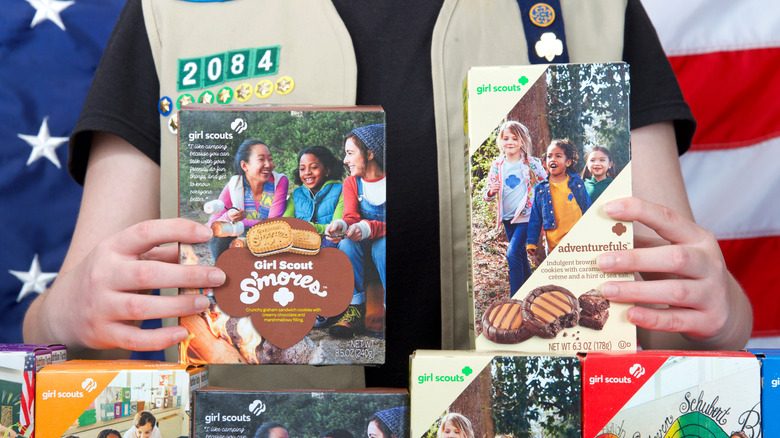 Girl Scout holding boxes of cookies in front of U.S. flag