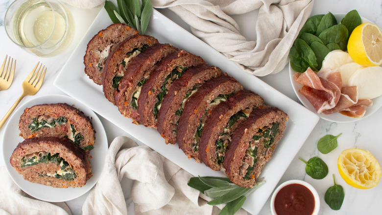 Saltimbocca-inspired spinach-stuffed meatloaf slices on serving platter next to more slices on plate
