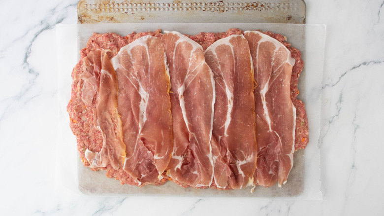 Prosciutto slices layered on top of flattened meatloaf mixture
