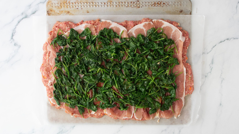 Flattened meatloaf mixture topped with prosciutto slices and sauteed spinach