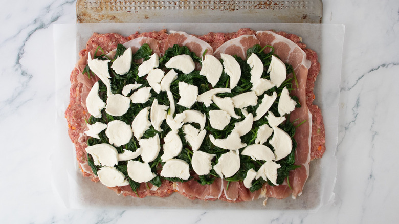 Flattened meatloaf mixture topped with prosciutto slices, sauteed spinach, and torn mozzarella