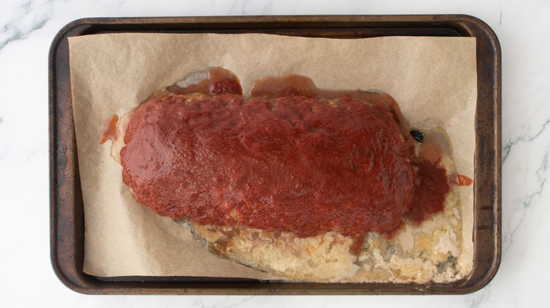 Meatloaf coated in tomato sauce on baking sheet