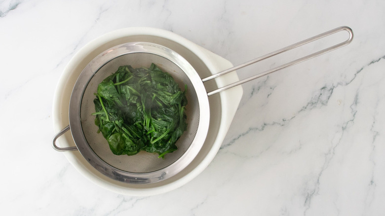 Wilted spinach draining in mesh sieve