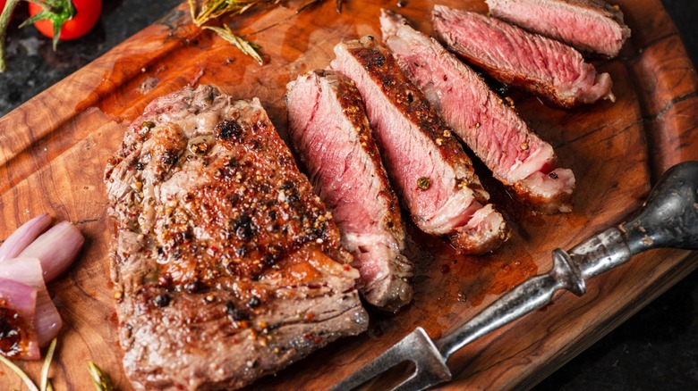 Cooked, partially sliced steak on a wooden cutting board