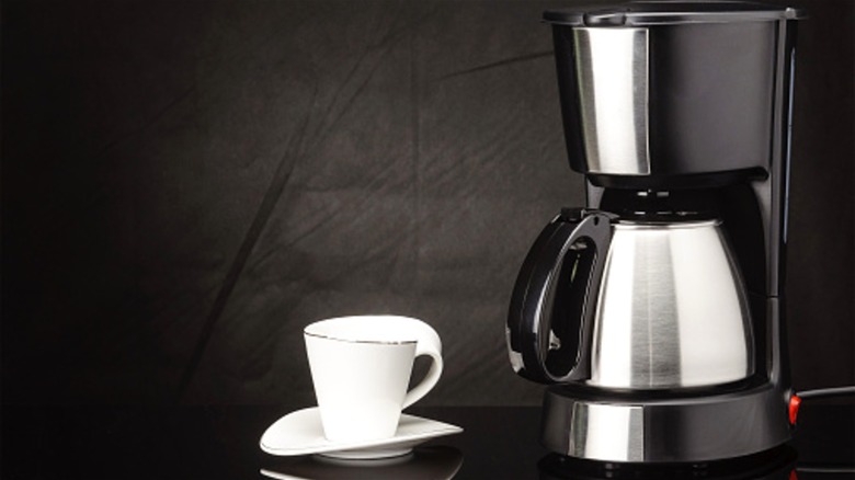 A coffee maker with a thermal carafe next to a white cup and saucer.